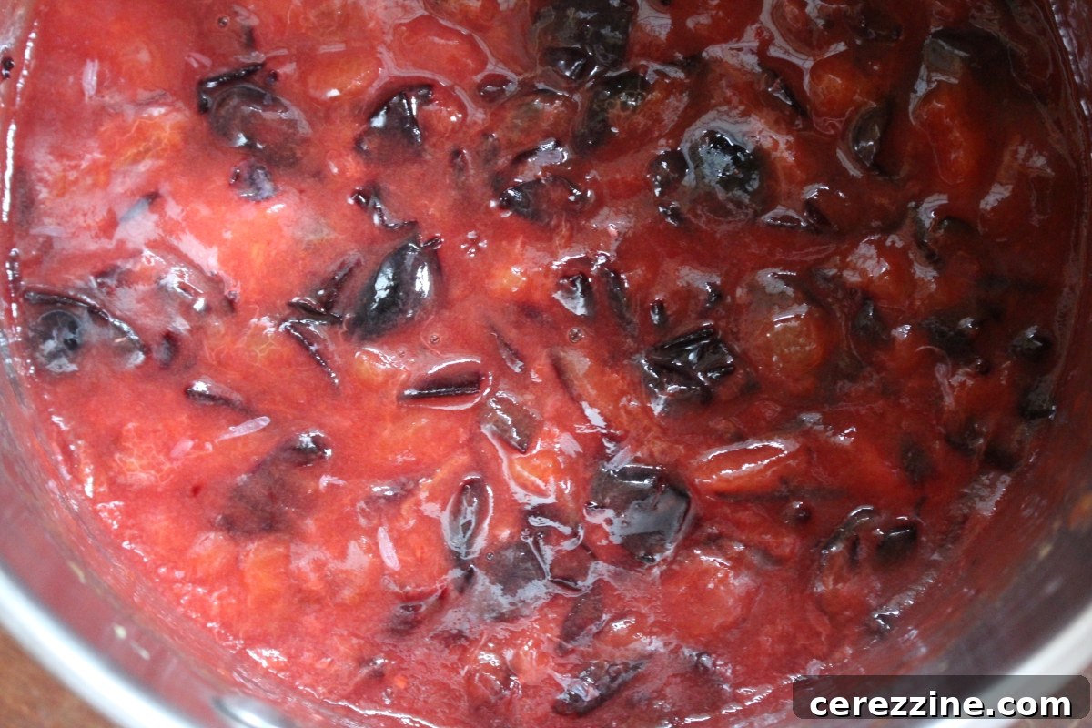 Damson jam simmering gently in a pot, just beginning to break down and thicken.