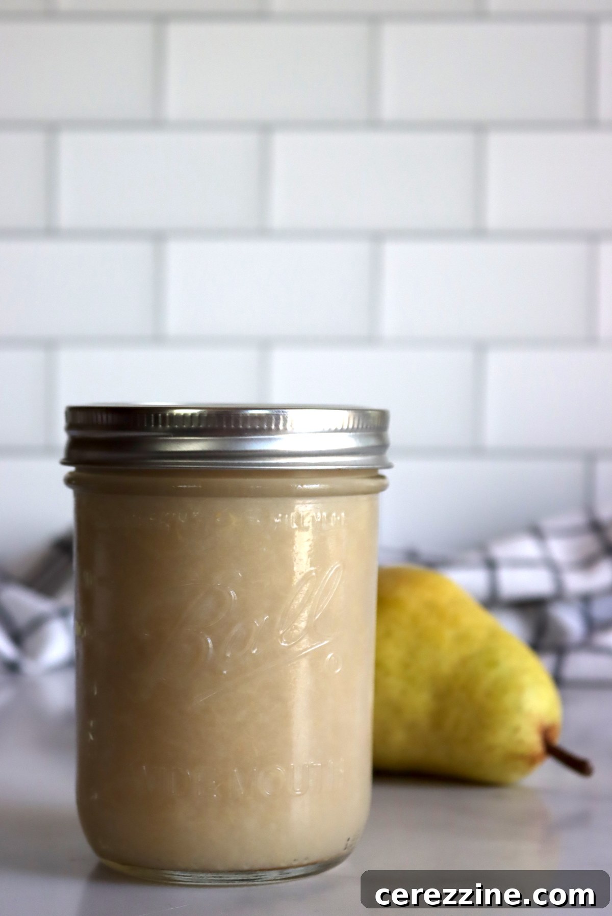 Smooth, white homemade pear sauce in a jar with fresh pears in the background.