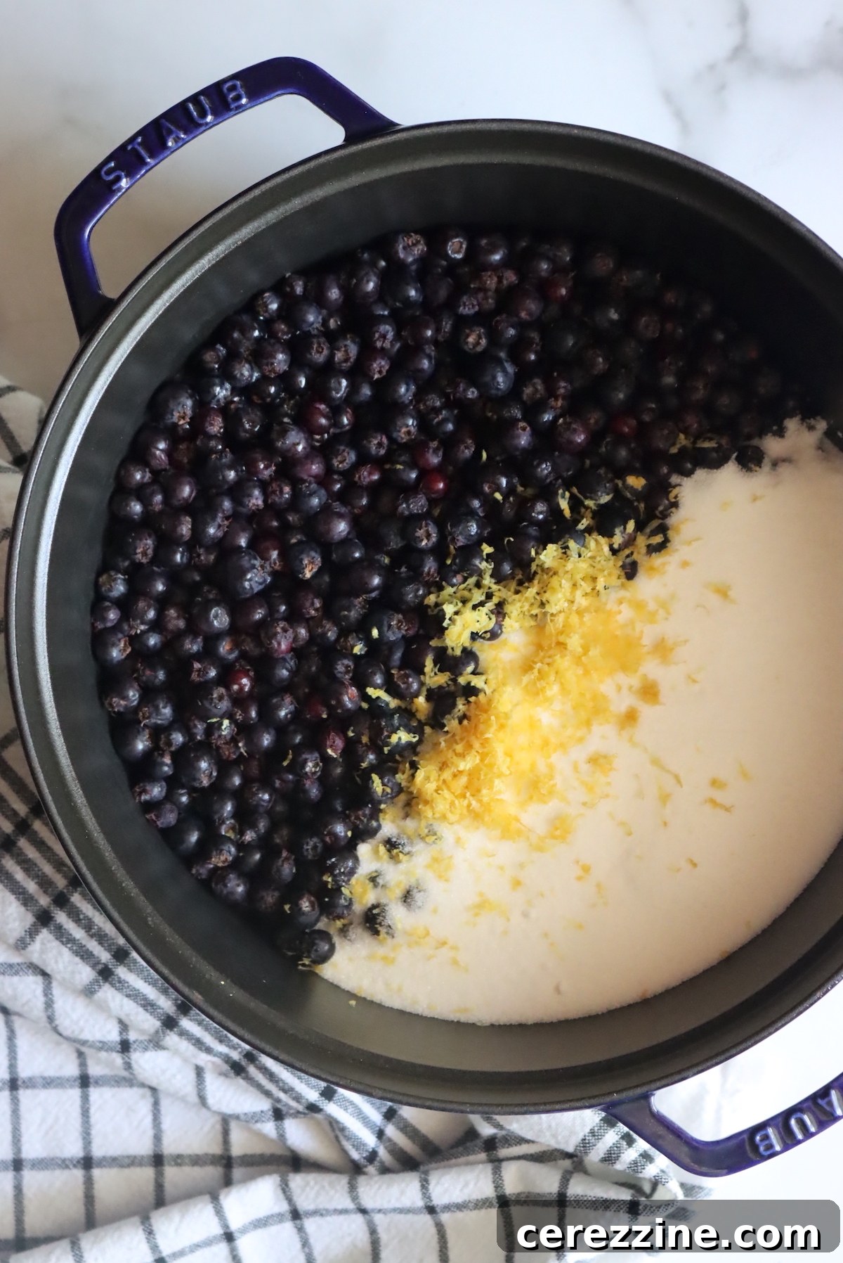 Ingredients for Saskatoon jam laid out on a wooden surface, including fresh berries, sugar, lemon, and a pot.