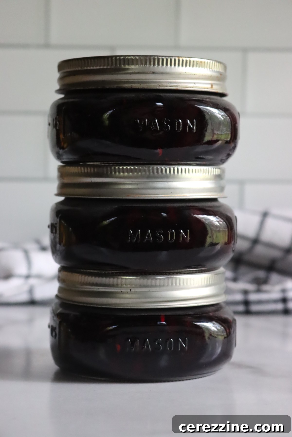 Sealed jars of homemade Saskatoon jam cooling on a counter after being removed from a water bath canner.