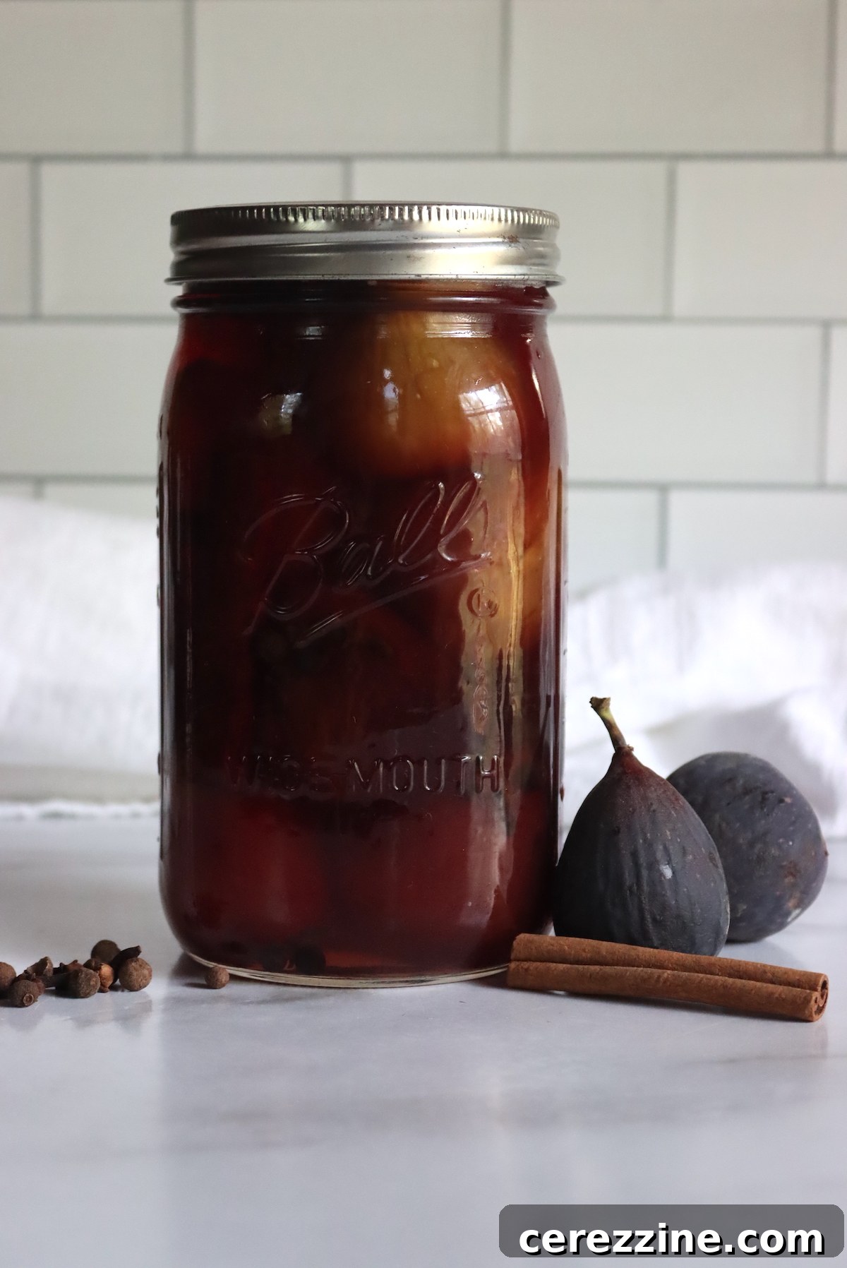 A hand gently placing a hot, freshly filled jar of pickled figs into a water bath canner.
