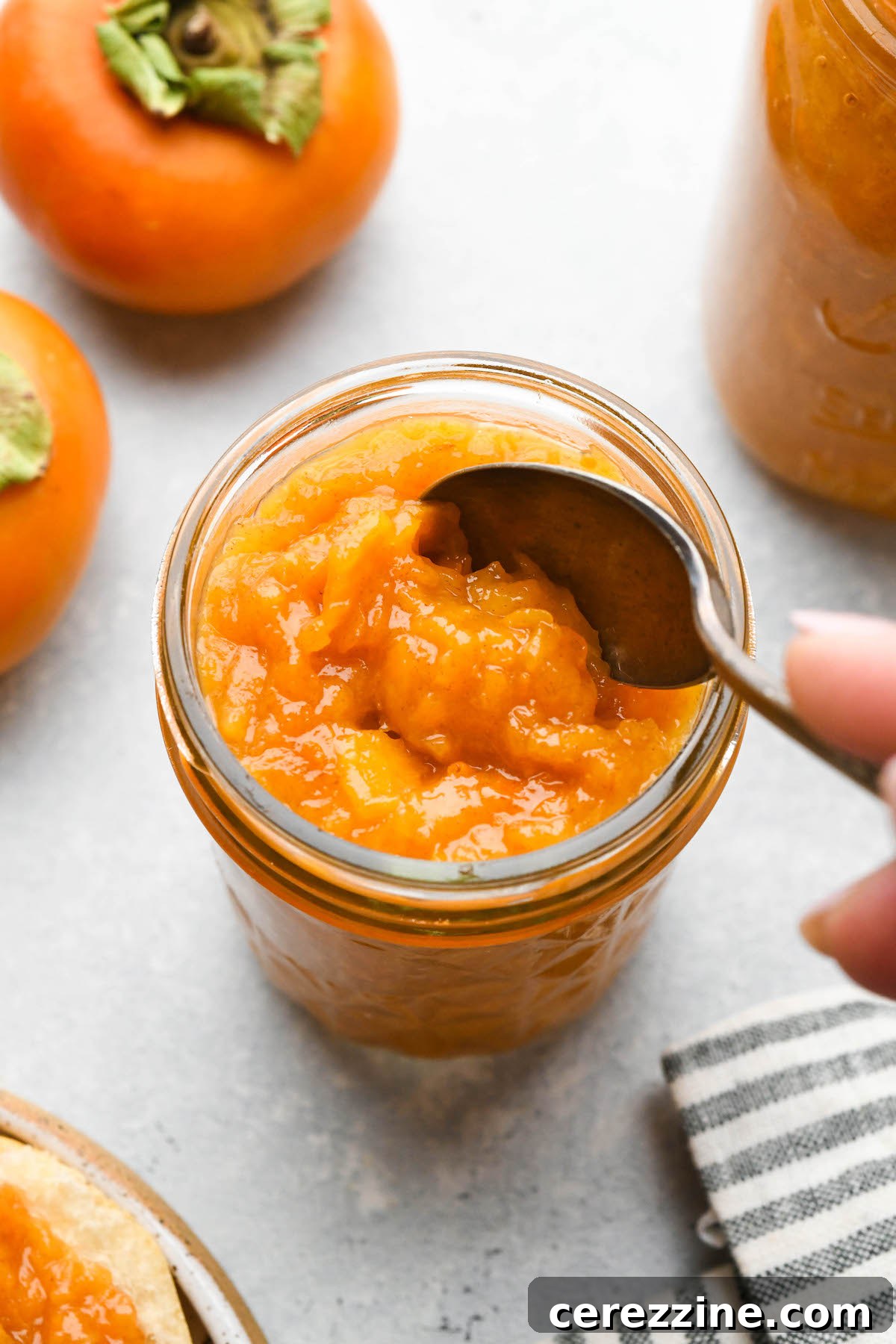 Freshly cooked persimmon jam being ladled into glass jars.