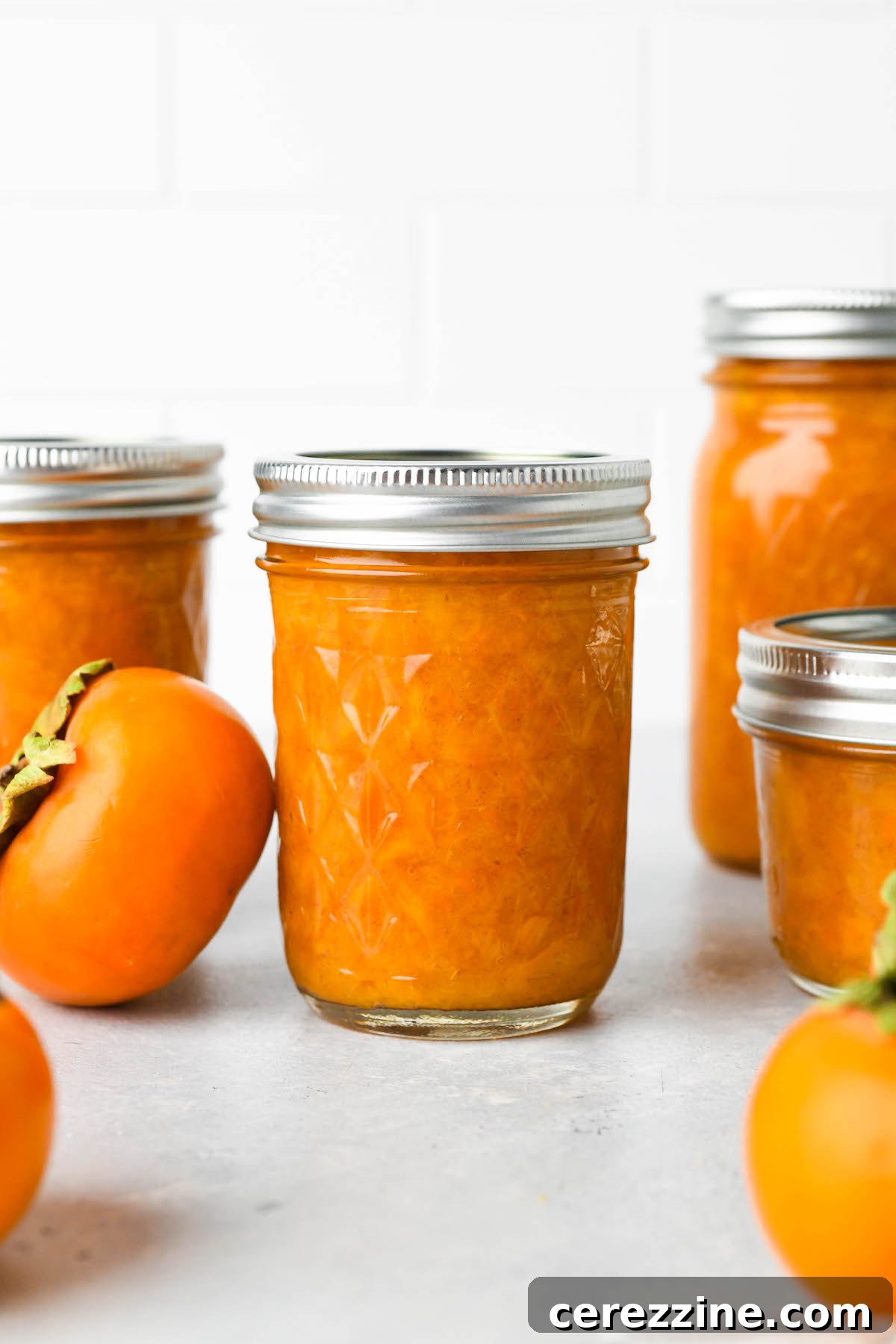 Canned persimmon jam jars cooling on a counter after water bath processing.