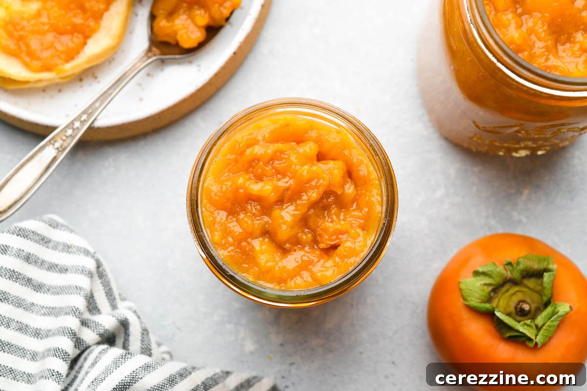 A jar of homemade persimmon jam next to a spoon with a dollop of jam.