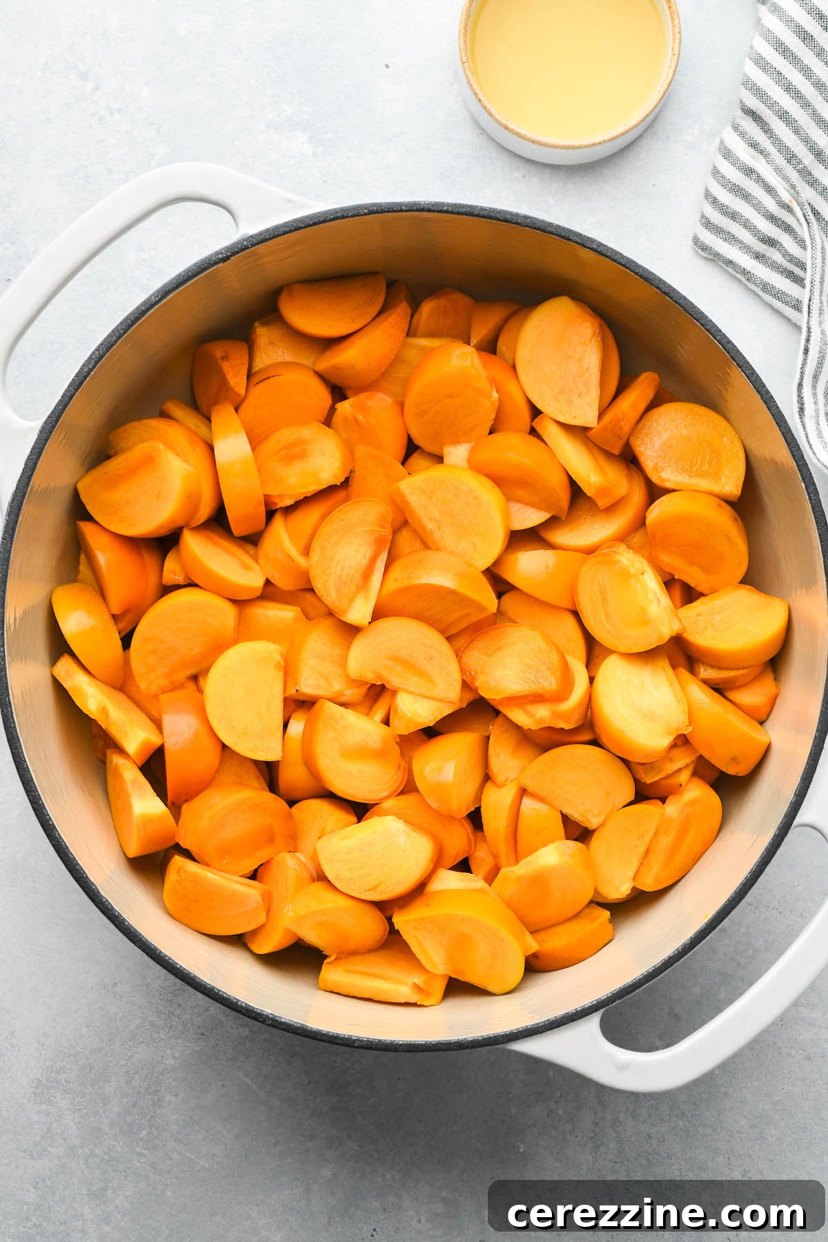 Persimmons simmering with lemon juice in a pot, breaking down for jam.