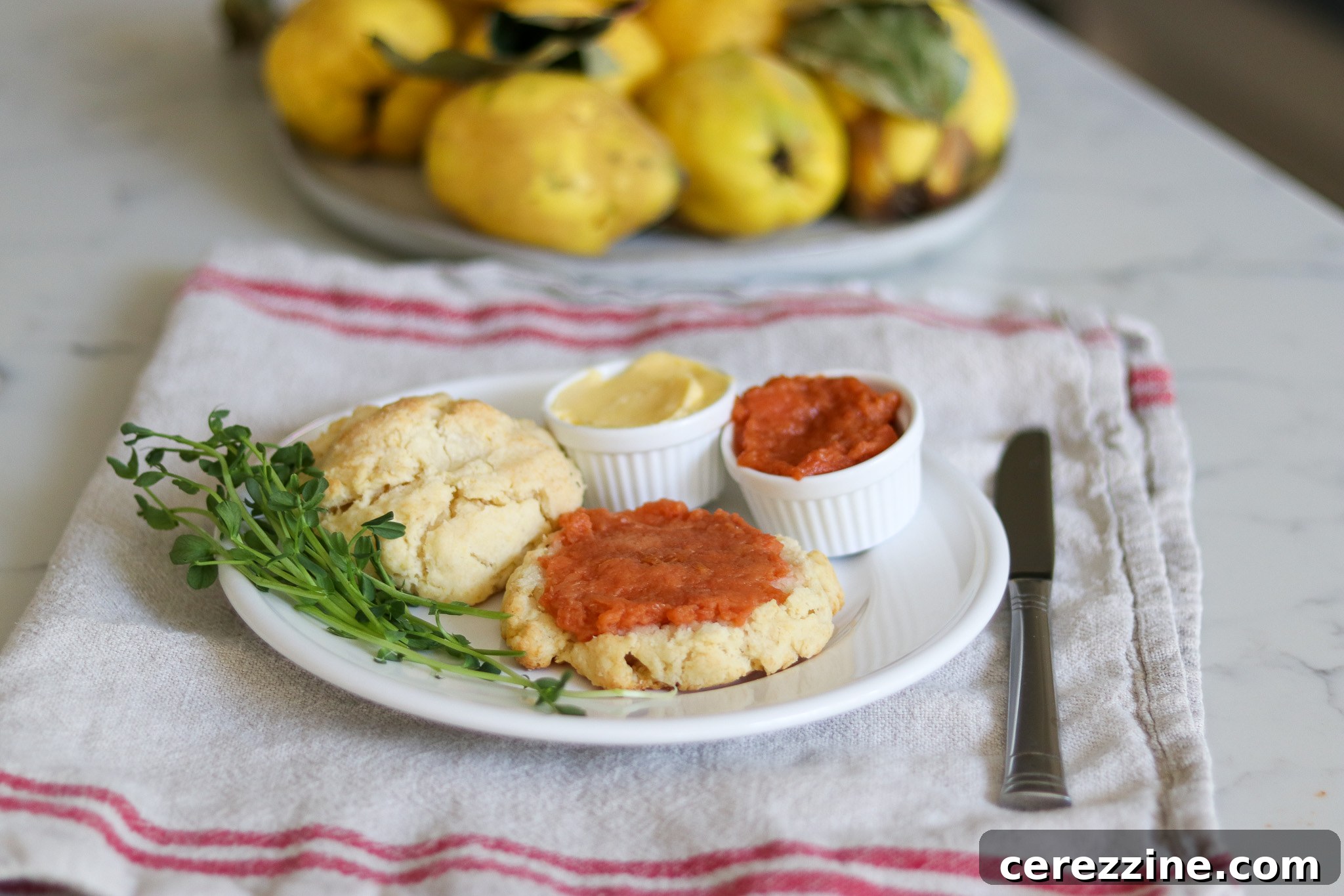 A serving of quince jam in a small bowl, garnished with a fresh quince slice, accompanied by cheese and crackers.