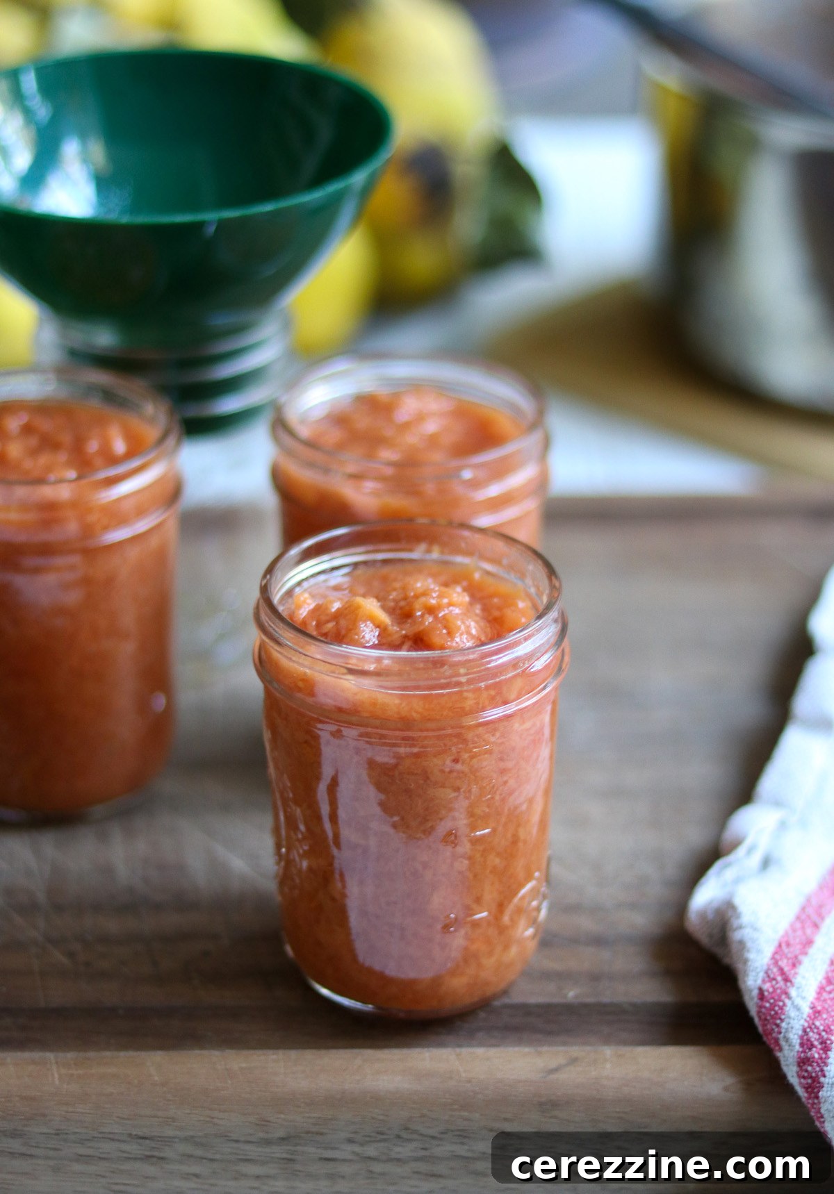 Close-up of vibrant pink quince jam glistening in a glass jar, showcasing its smooth texture.