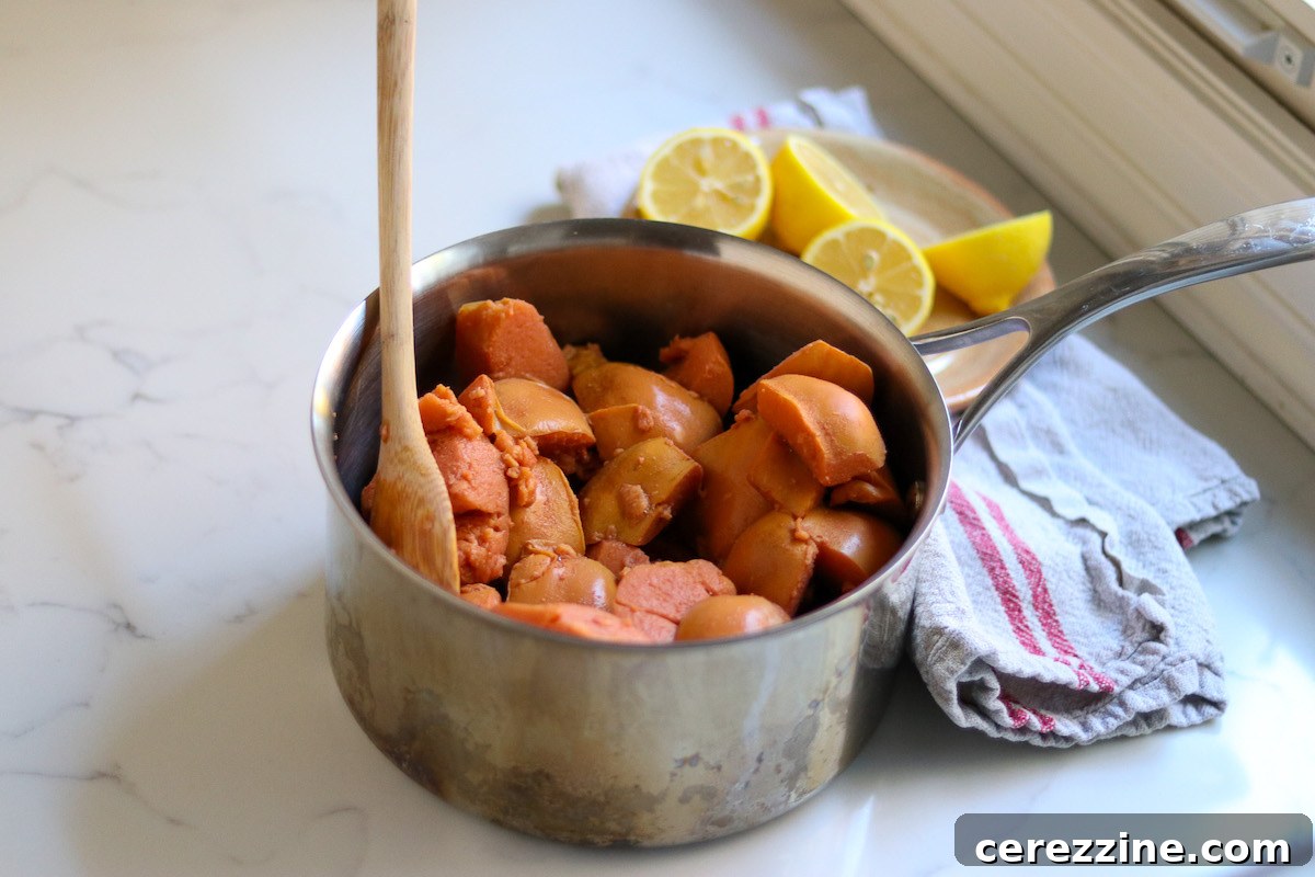 Diced quince pieces simmering in a saucepan with water, turning pink as they cook.