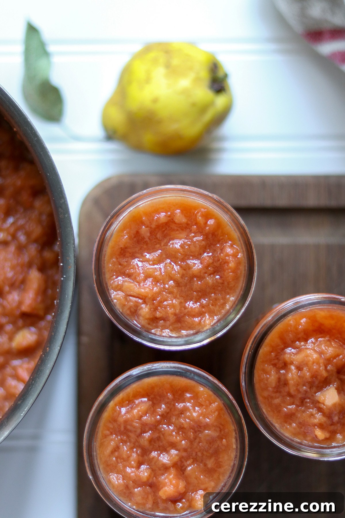 Rows of freshly canned quince jam jars cooling on a towel, showcasing their beautiful pink color.