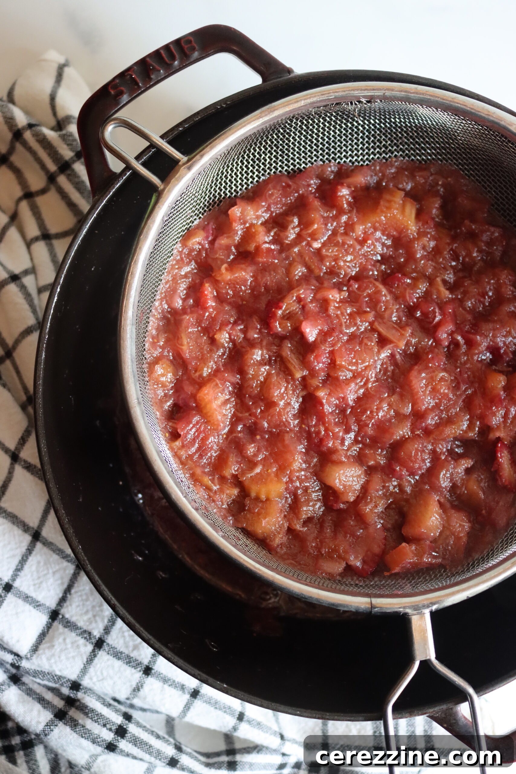 Straining strawberry and rhubarb pulp from the juice using a colander over a bowl.