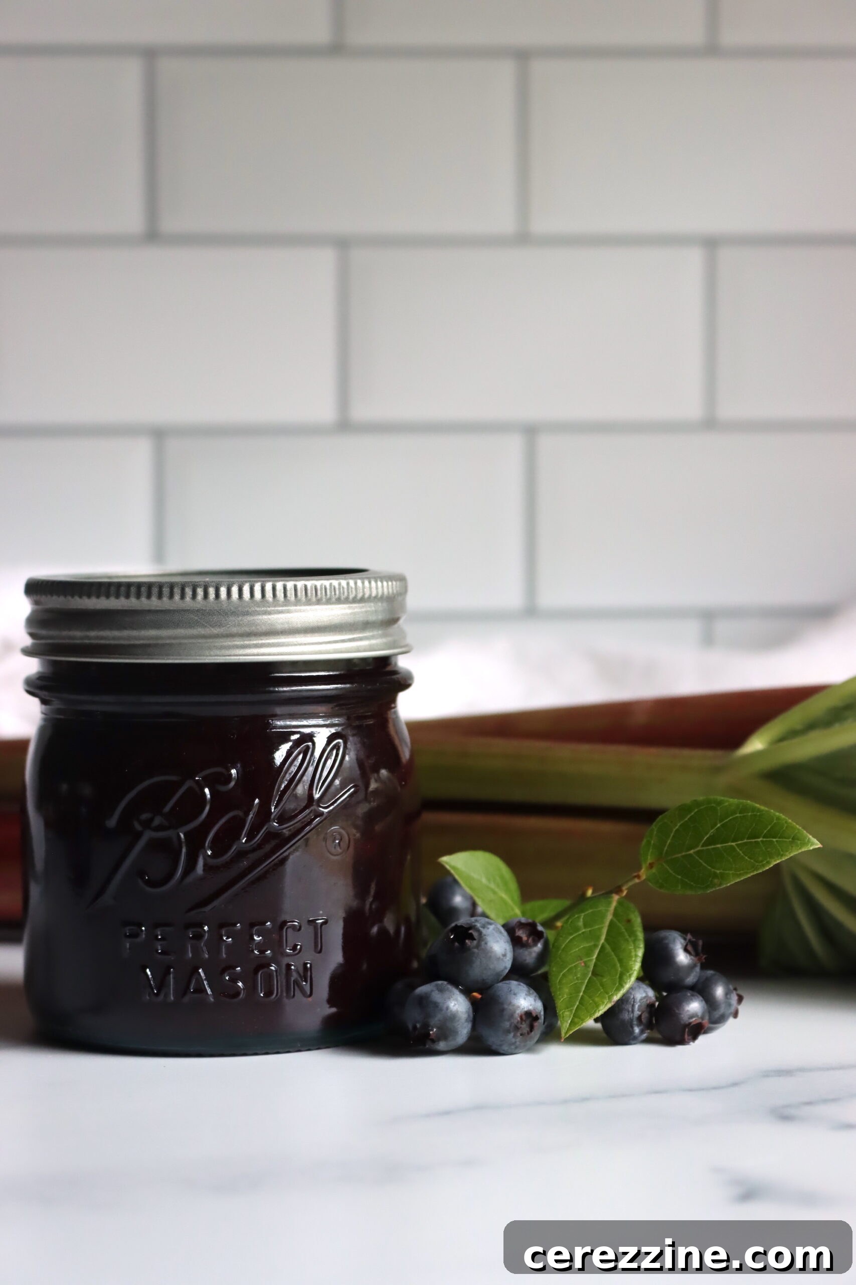 Jars of blueberry rhubarb jam being removed from a water bath canner with a jar lifter