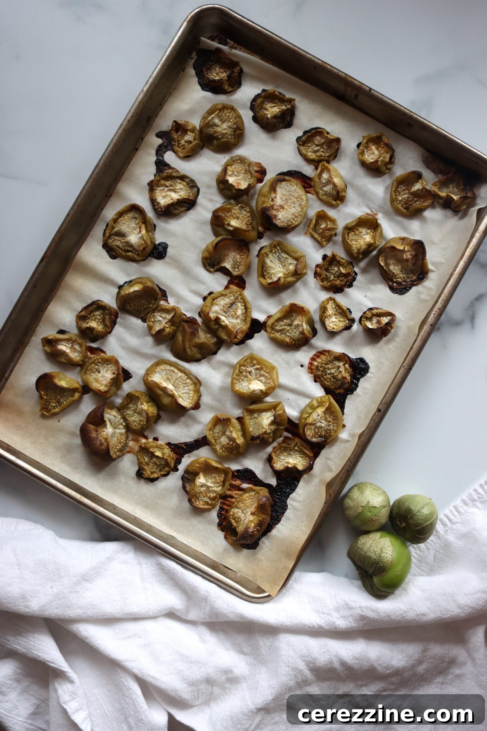 Zesty Chipotle Verde 5 Roasted tomatillos and onions on a baking sheet, showing some charring