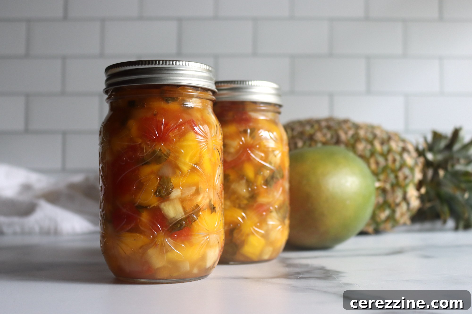Glass jars filled with Pineapple Mango Salsa, ready for water bath canning.