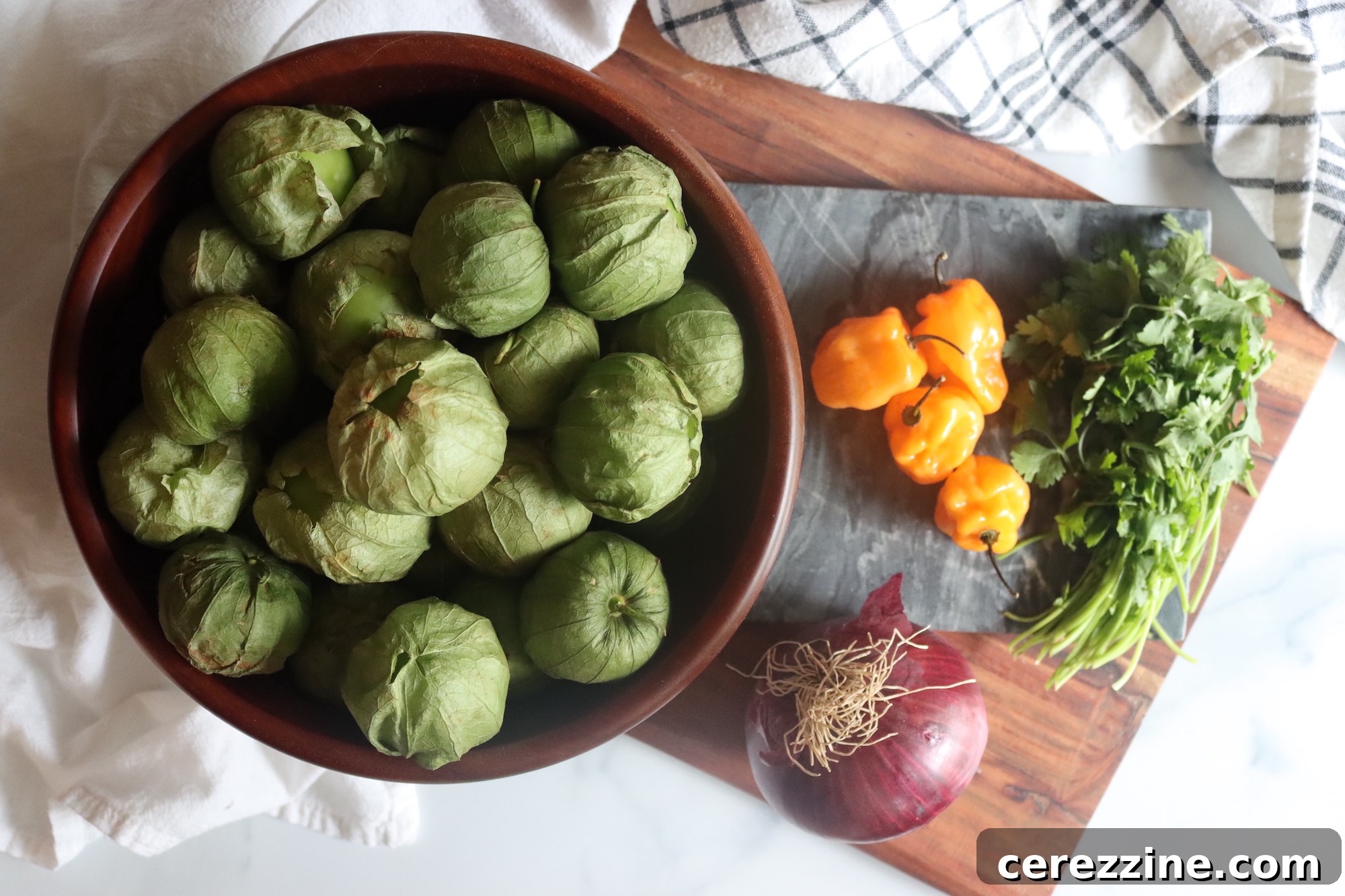 Fresh ingredients laid out: tomatillos, habaneros, red onion, cilantro, and lime.