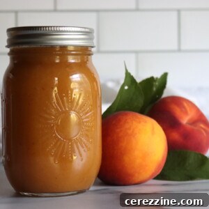 Two jars of peach nectar on a white countertop with a white tile background, with two fresh peaches next to them.