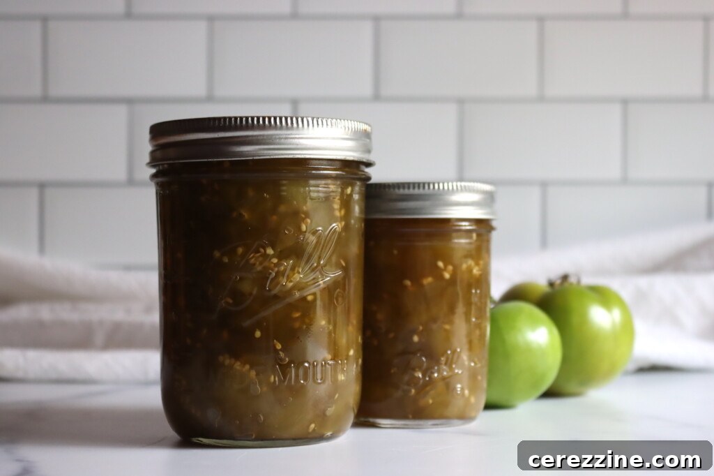 Two jars of glistening Canadian Green Tomato Chow Chow, with fresh green tomatoes scattered nearby, set against a clean white background.