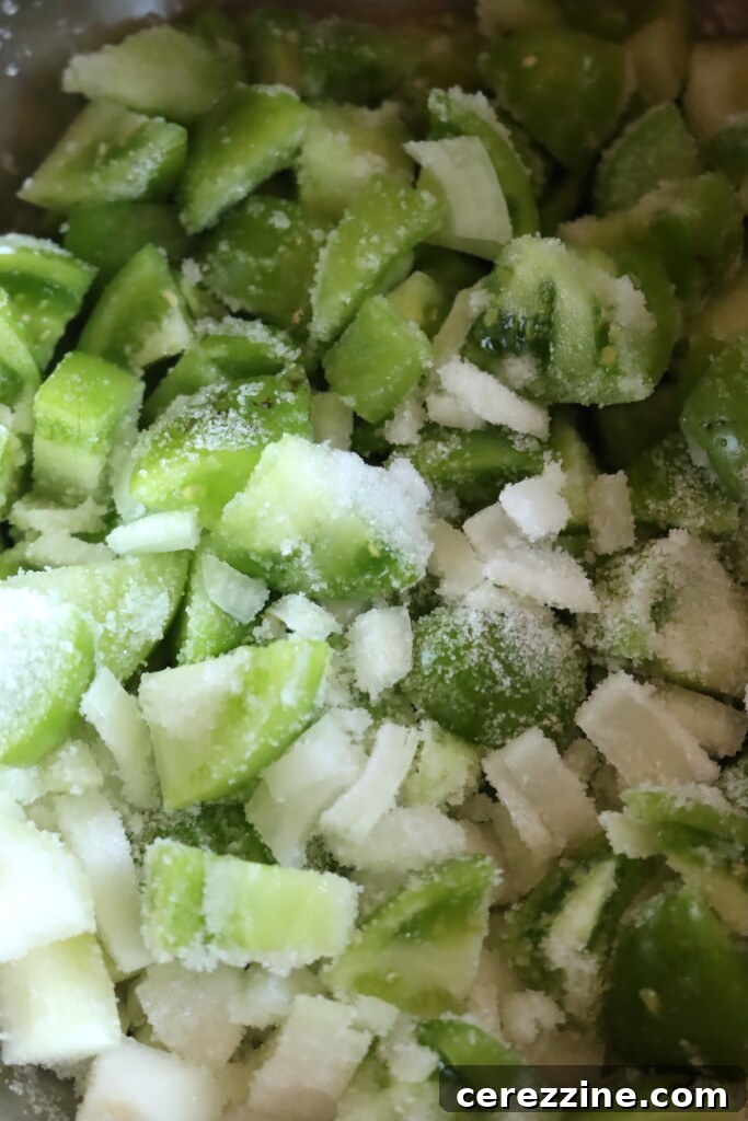 A close-up view of salted green tomatoes and onions resting in a colander, ready for their overnight moisture release.