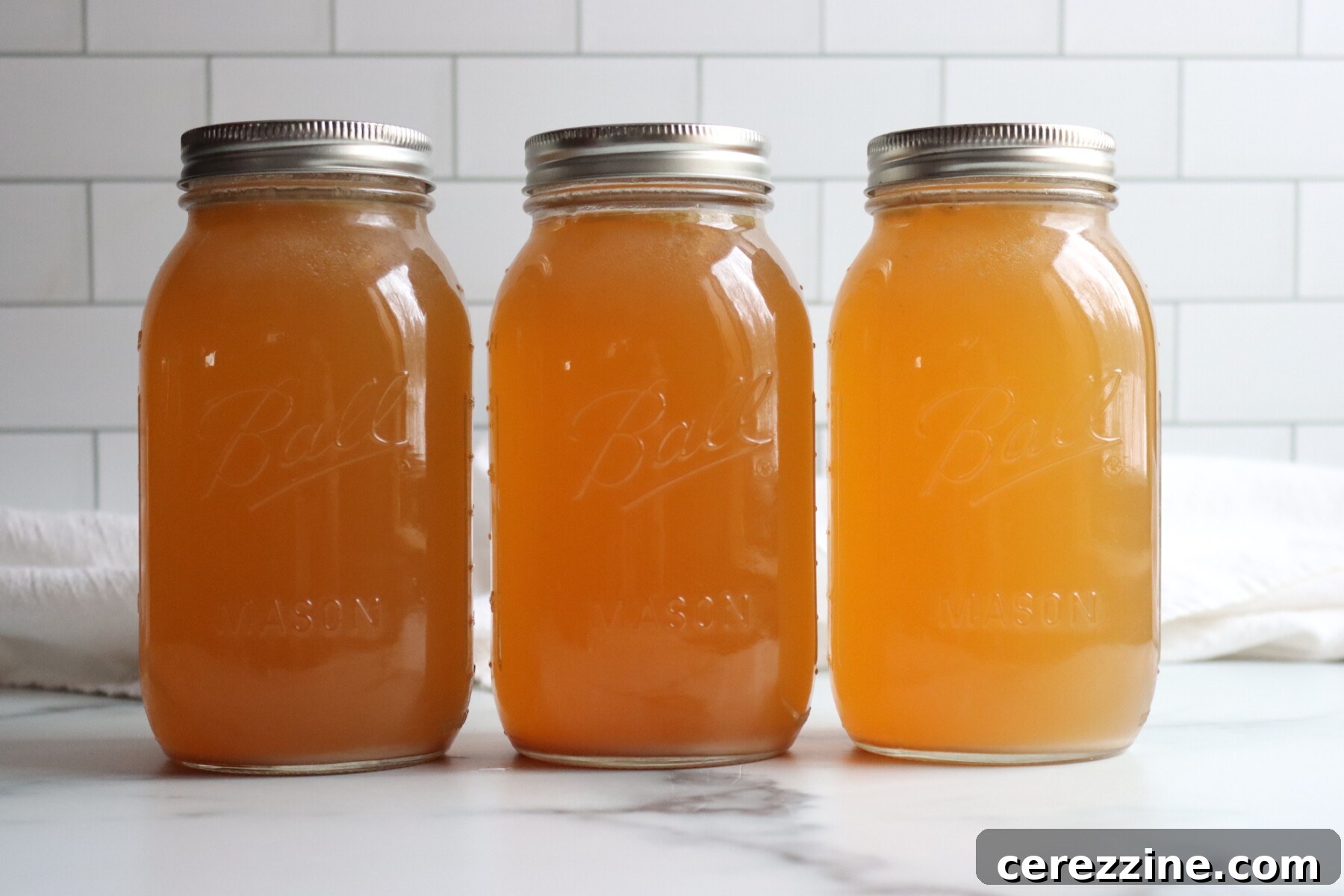 Three jars of turkey broth in a line on a white counter.