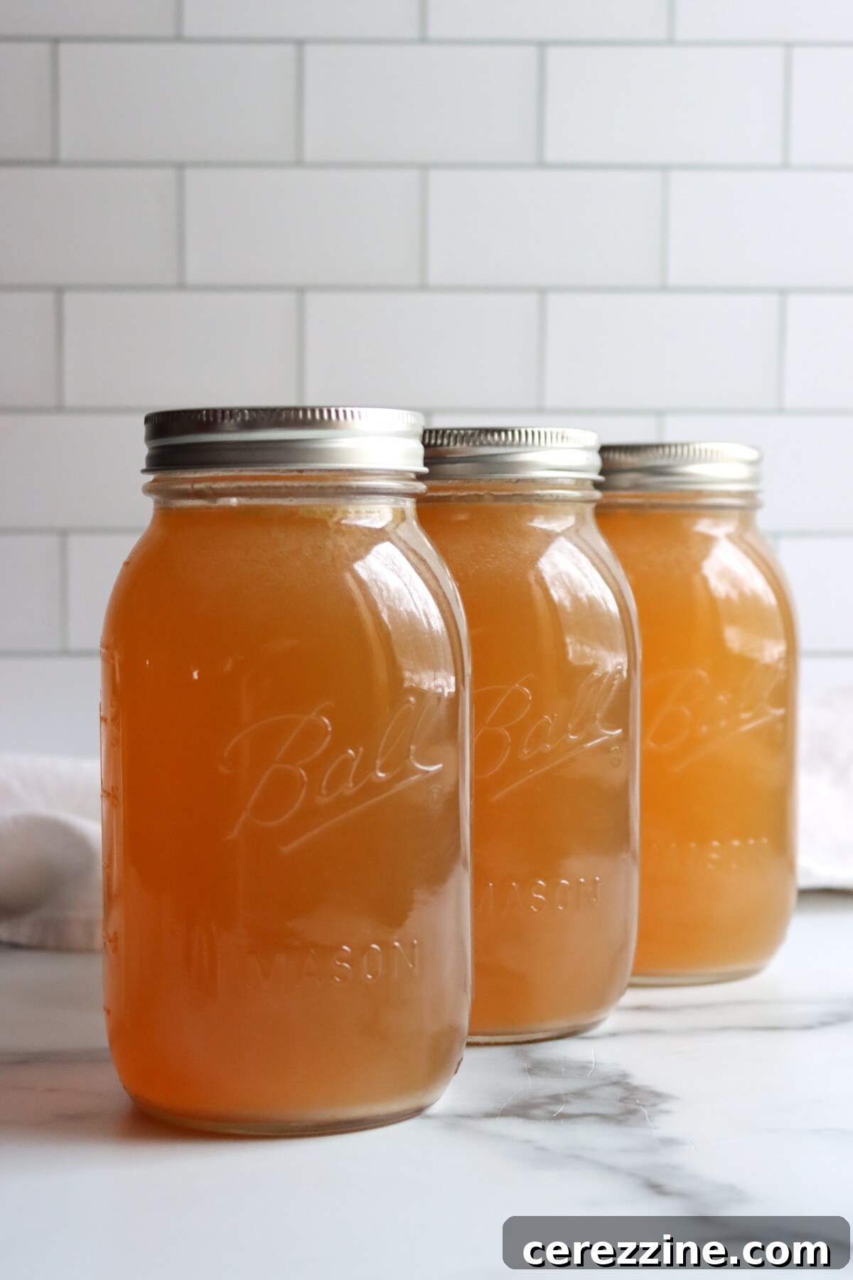 Three quart jars of pressure canned turkey stock on a white counter.