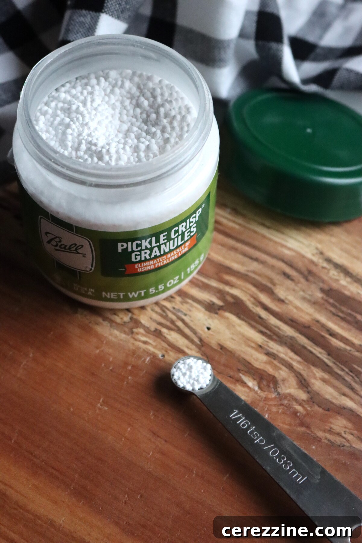 Home Canning Perfection The Calcium Chloride Crunch 5 Pickle Crisp Amount in a 1/16th tsp measuring spoon on a cutting board.