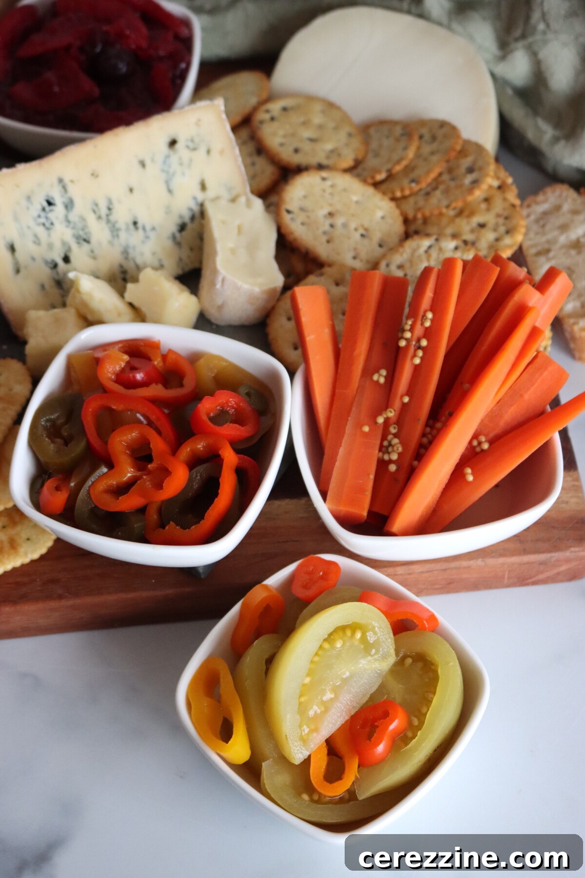 Spicy pickled green tomatoes served on a cheese board with sweet pickled carrots and pickled peppers.