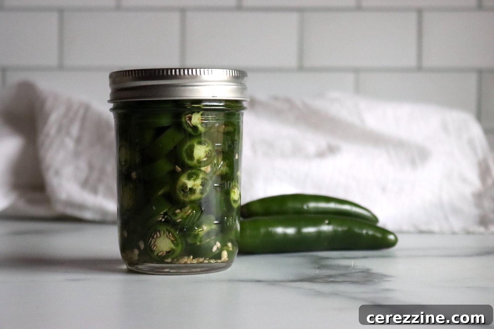 Pickled Serrano Peppers Recipe: Spicy Refrigerator Pickles 2 Jar of pickled serrano peppers with two fresh serranos beside it on a marble counter