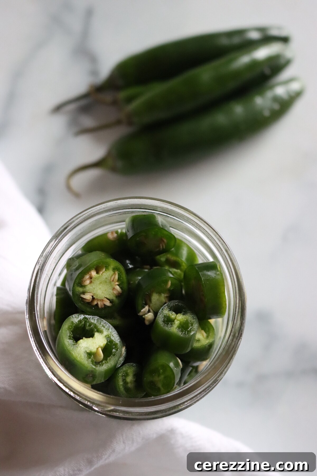 Pickled Serrano Peppers Recipe: Spicy Refrigerator Pickles 4 Open jar of sliced pickled serrano peppers seen from above, with fresh whole serranos beside it