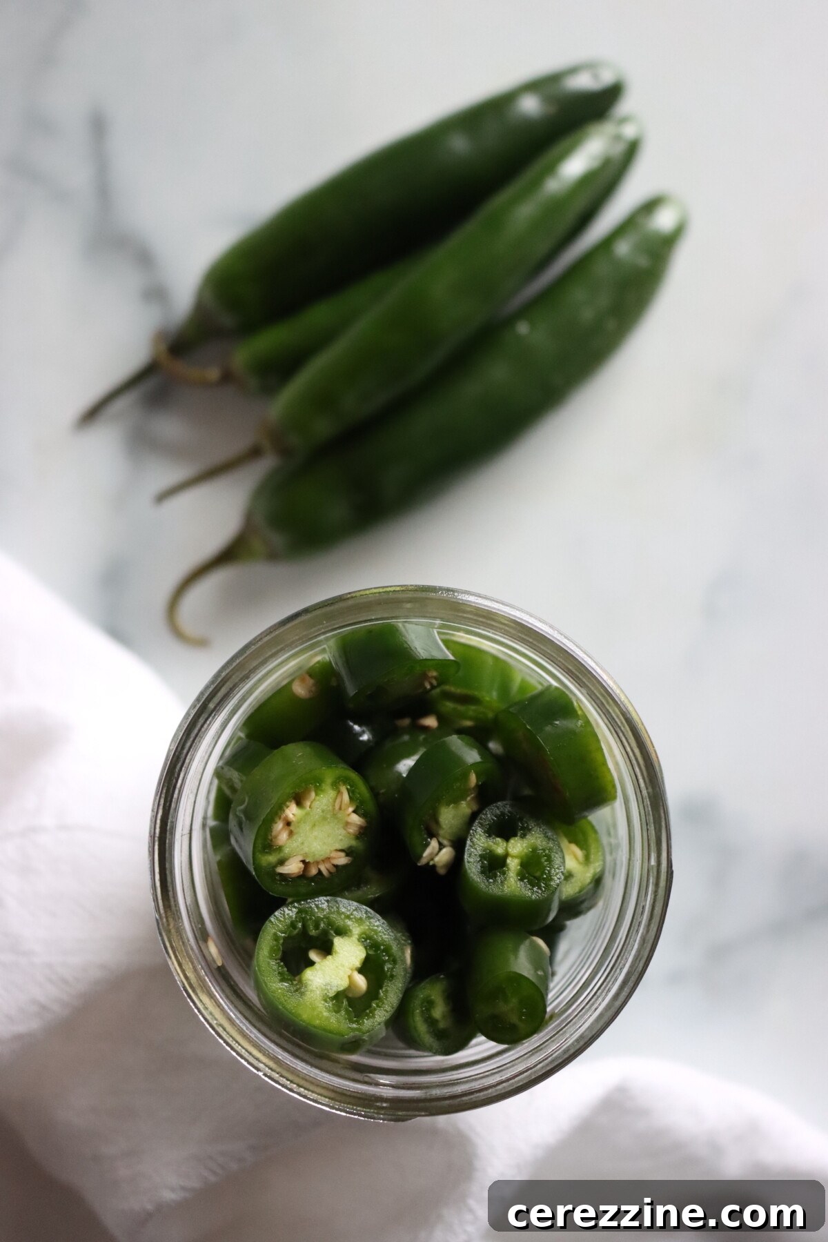 Pickled Serrano Peppers Recipe: Spicy Refrigerator Pickles 5 Serrano pepper rings packed in an open jar, seen from above, next to fresh serrano peppers