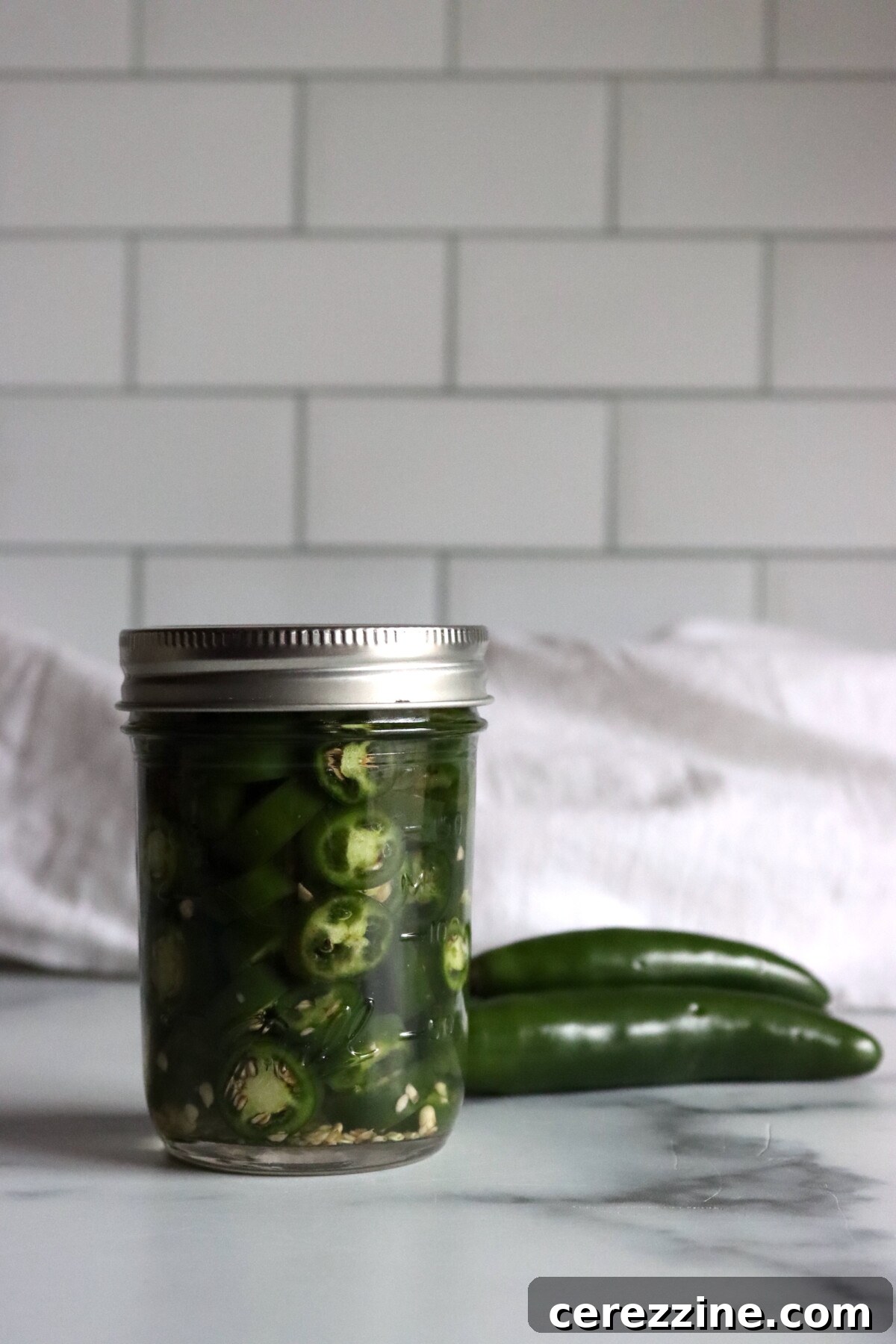 Pickled Serrano Peppers Recipe: Spicy Refrigerator Pickles 6 Sealed jar of pickled serrano pepper rings in brine with whole serrano peppers on the counter