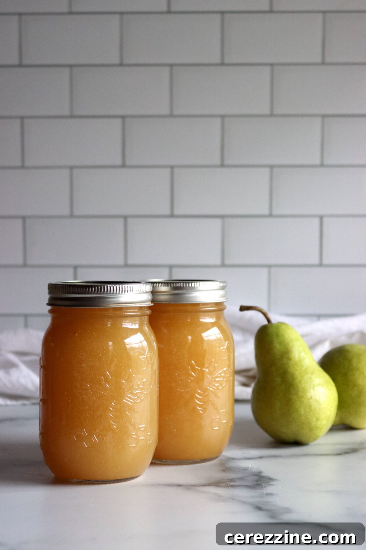 Two pint jars of homemade pear honey beside fresh pears