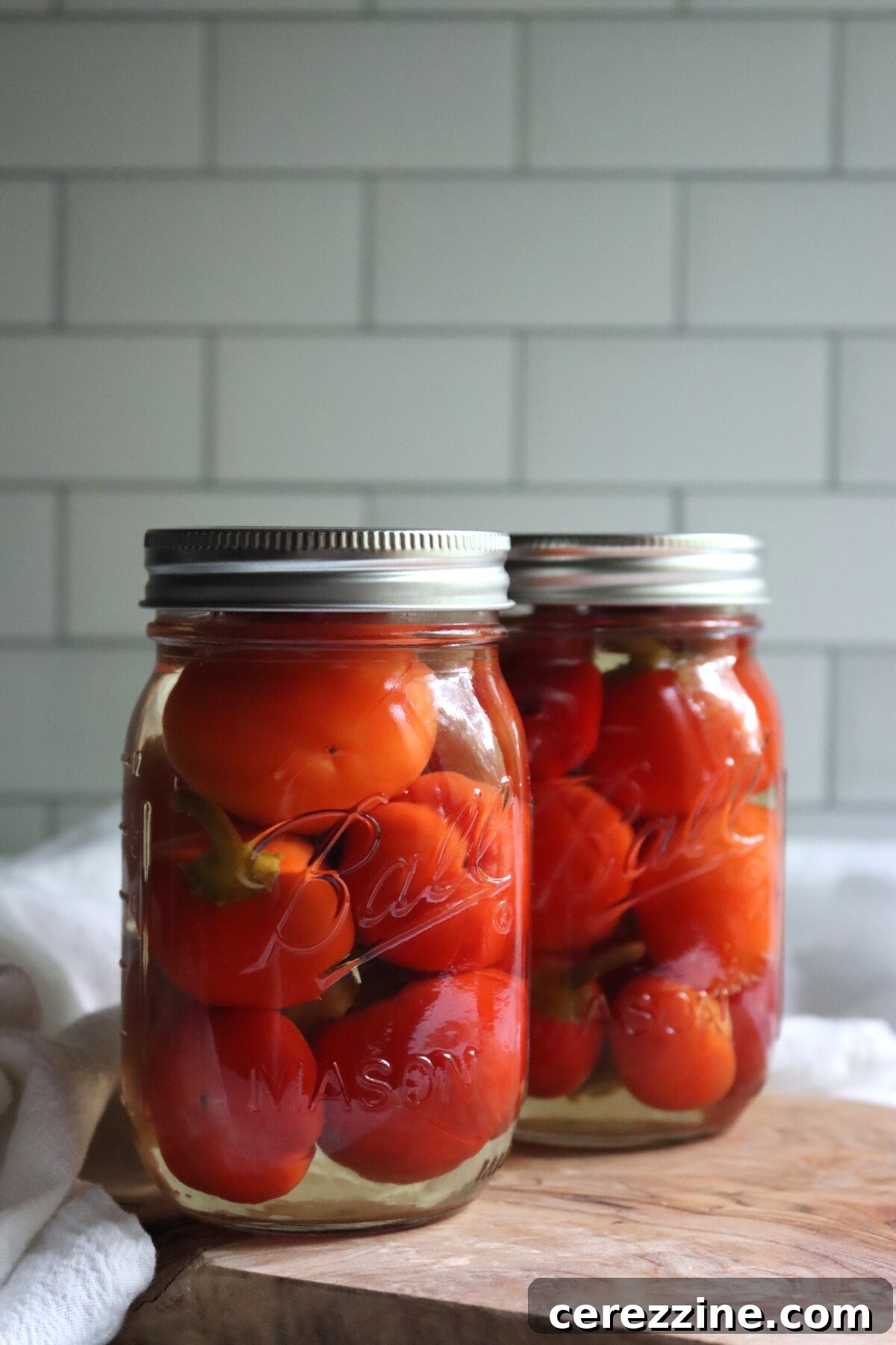 Close-up of two jars of pickled cherry peppers, packed whole in a vinegar brine