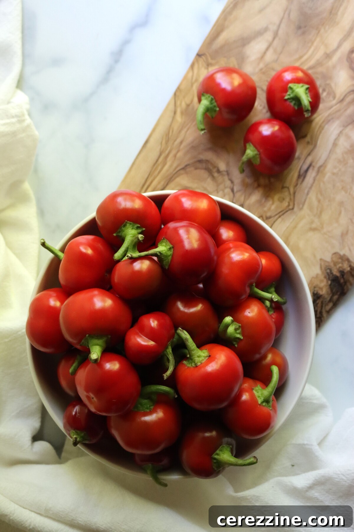 A bowl of fresh red cherry peppers on a wooden cutting board, ready for pickling
