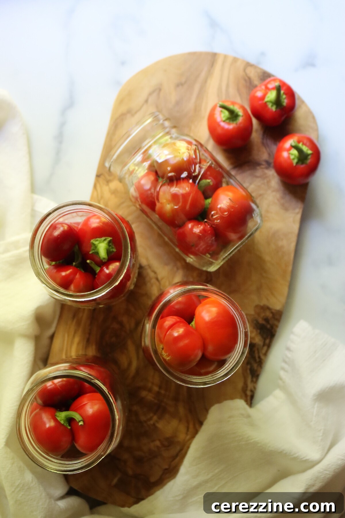 Overhead view of whole cherry peppers being packed into pint jars for pickling