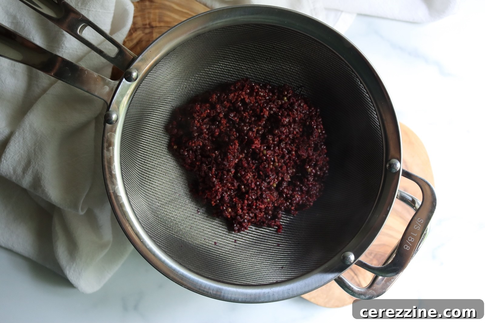 Cooked elderberries draining in a fine-mesh strainer to make elderberry juice