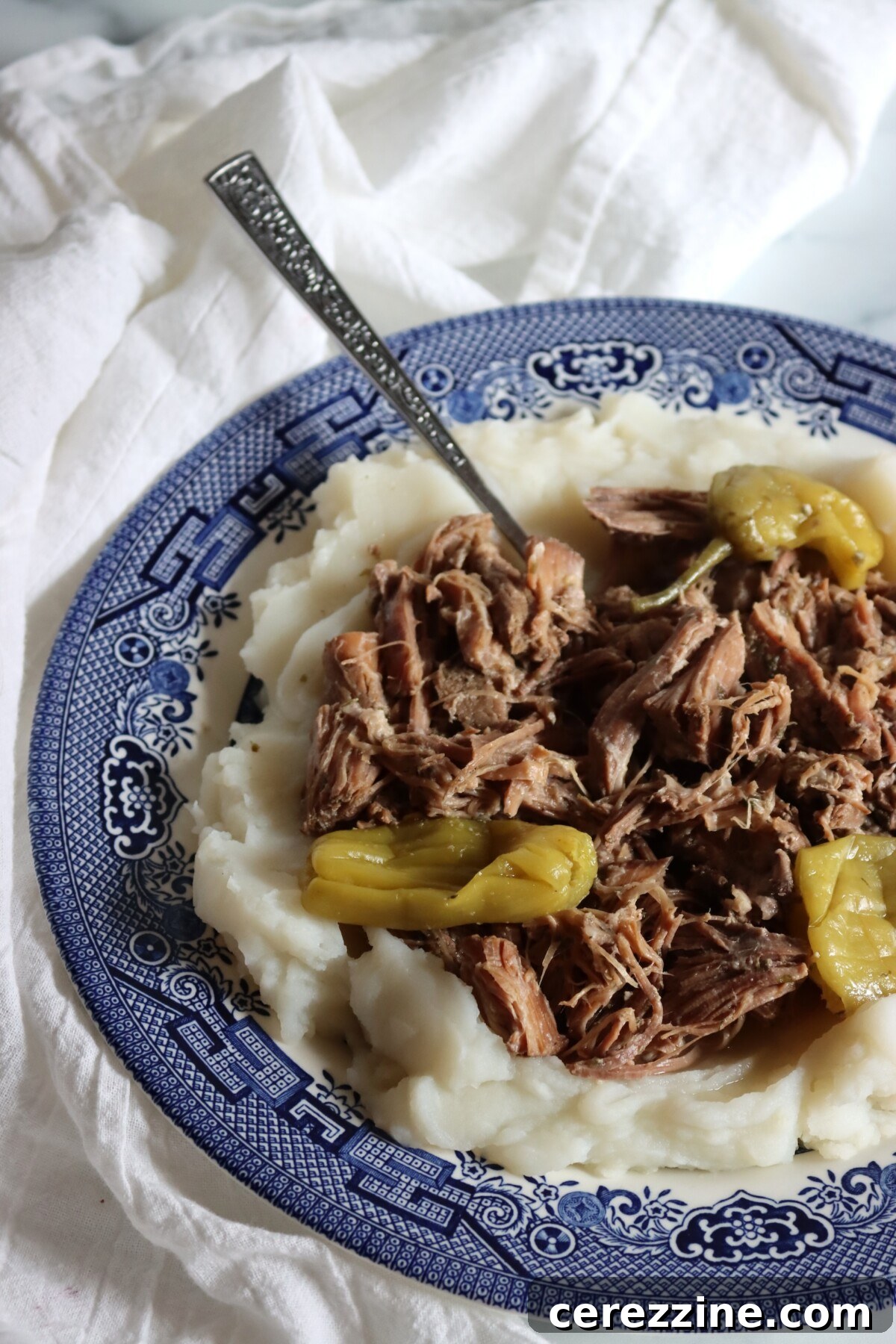 Close-up of shredded pork and pepperoncini over mashed potatoes on a blue and white plate