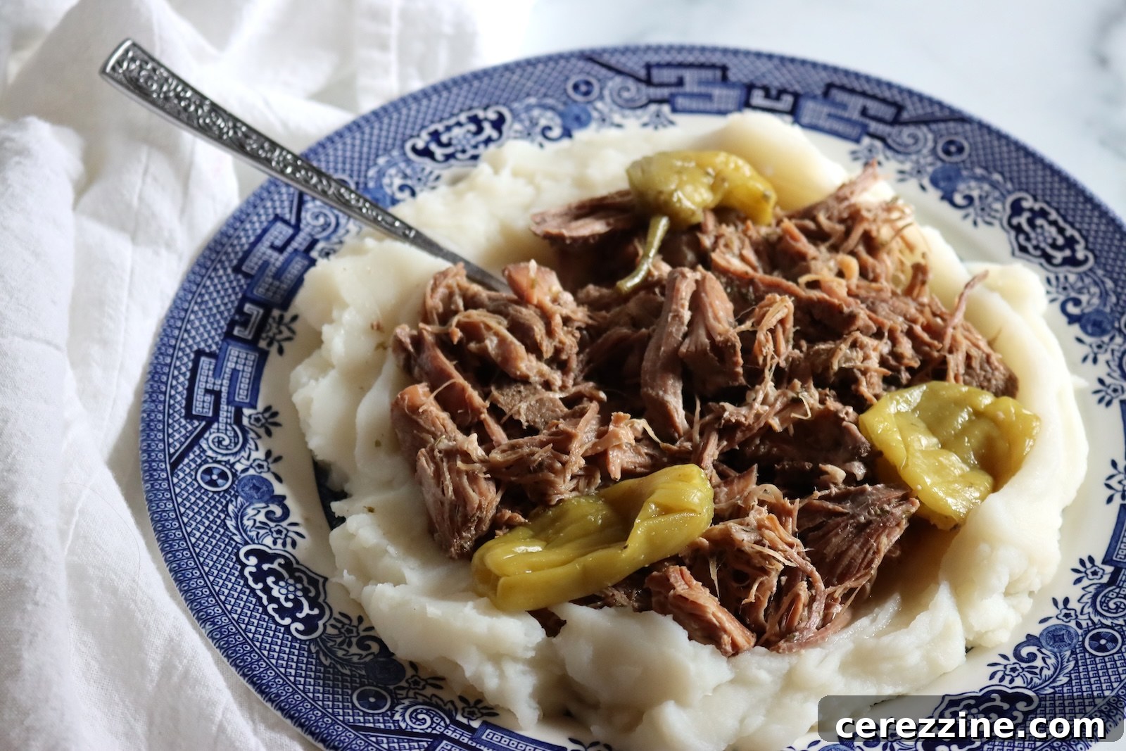 A plate of Mississippi pork roast with pepperoncini over mashed potatoes, made from a canned jar