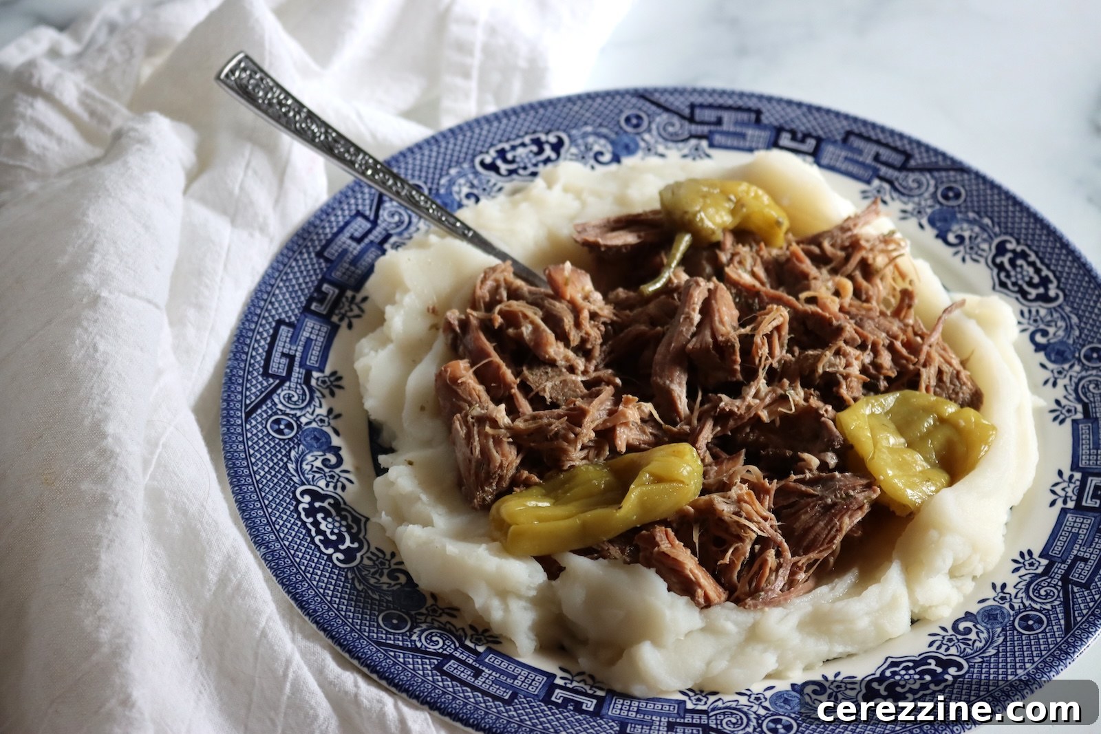 Shredded Mississippi pork roast and pepperoncini on a blue and white plate of mashed potatoes