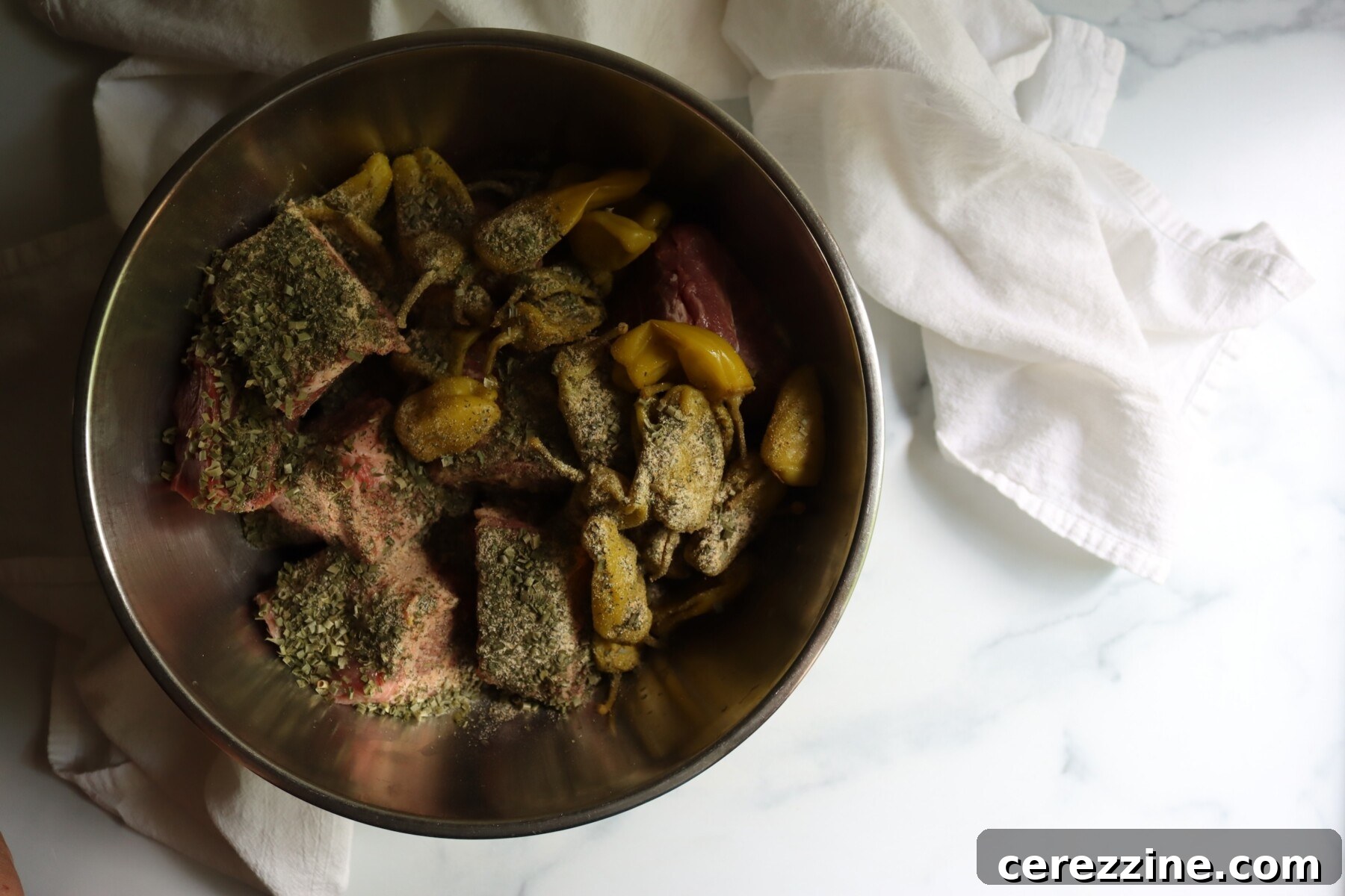 Cubed pork shoulder tossed with pepperoncini and dried ranch herbs in a stainless steel bowl
