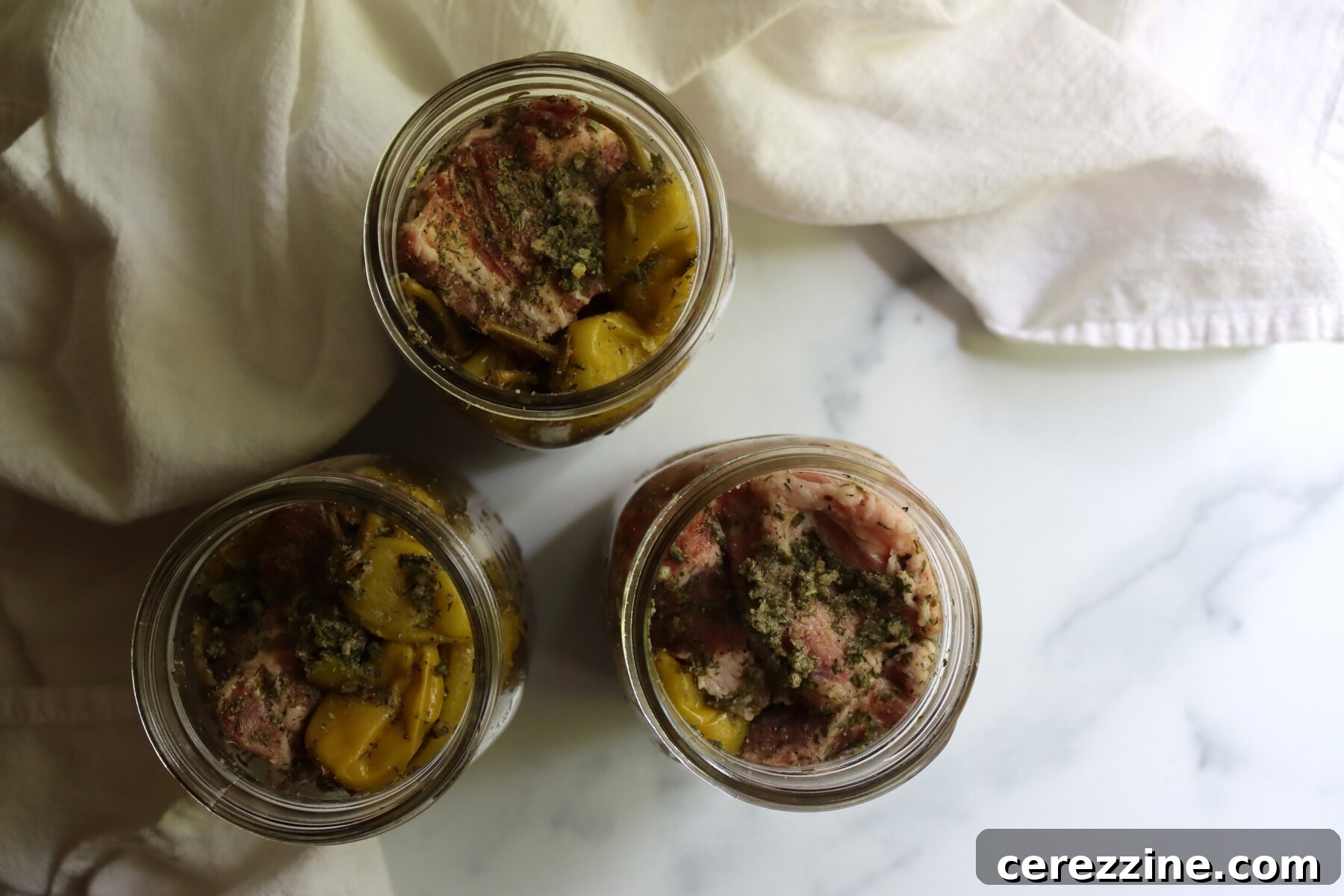 Three quart jars packed with raw pork, pepperoncini, and herbs, ready for the pressure canner