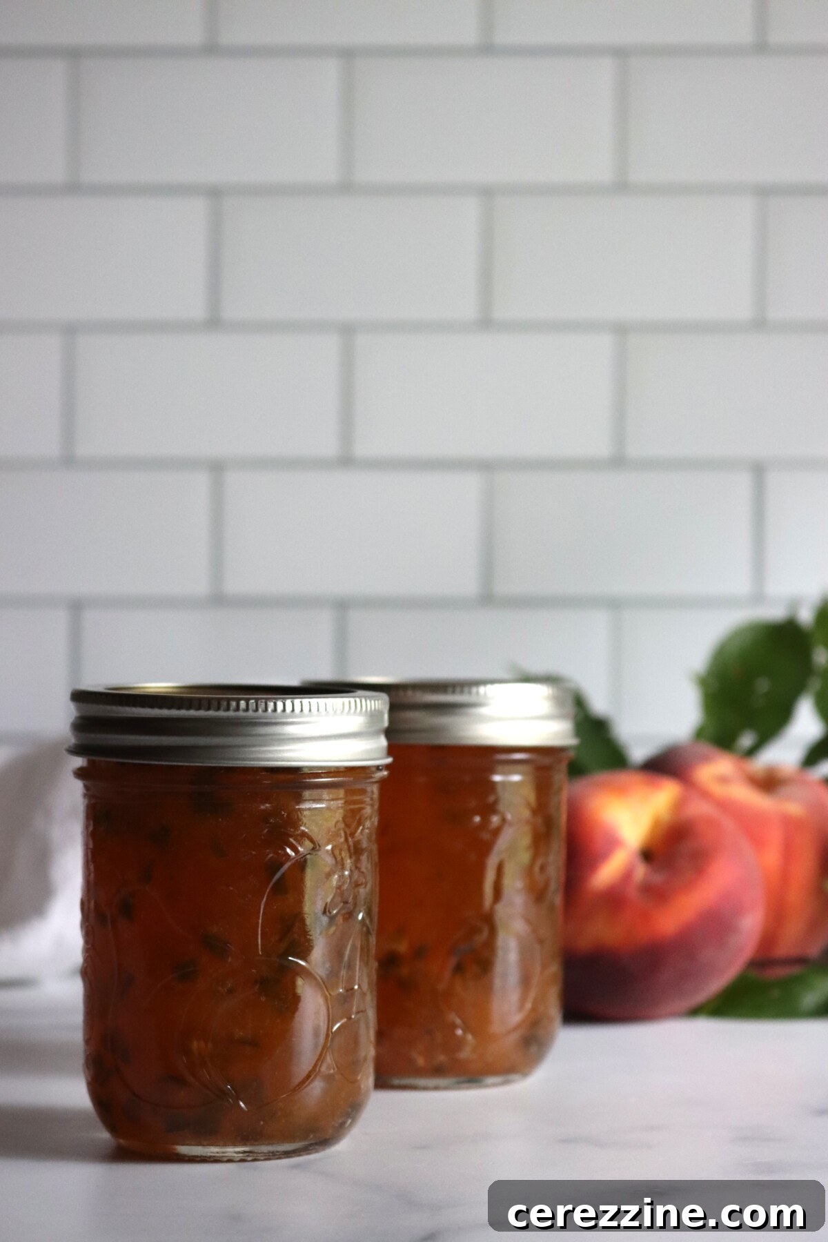 Peach jalapeño jam in half-pint jars with a halved peach behind them