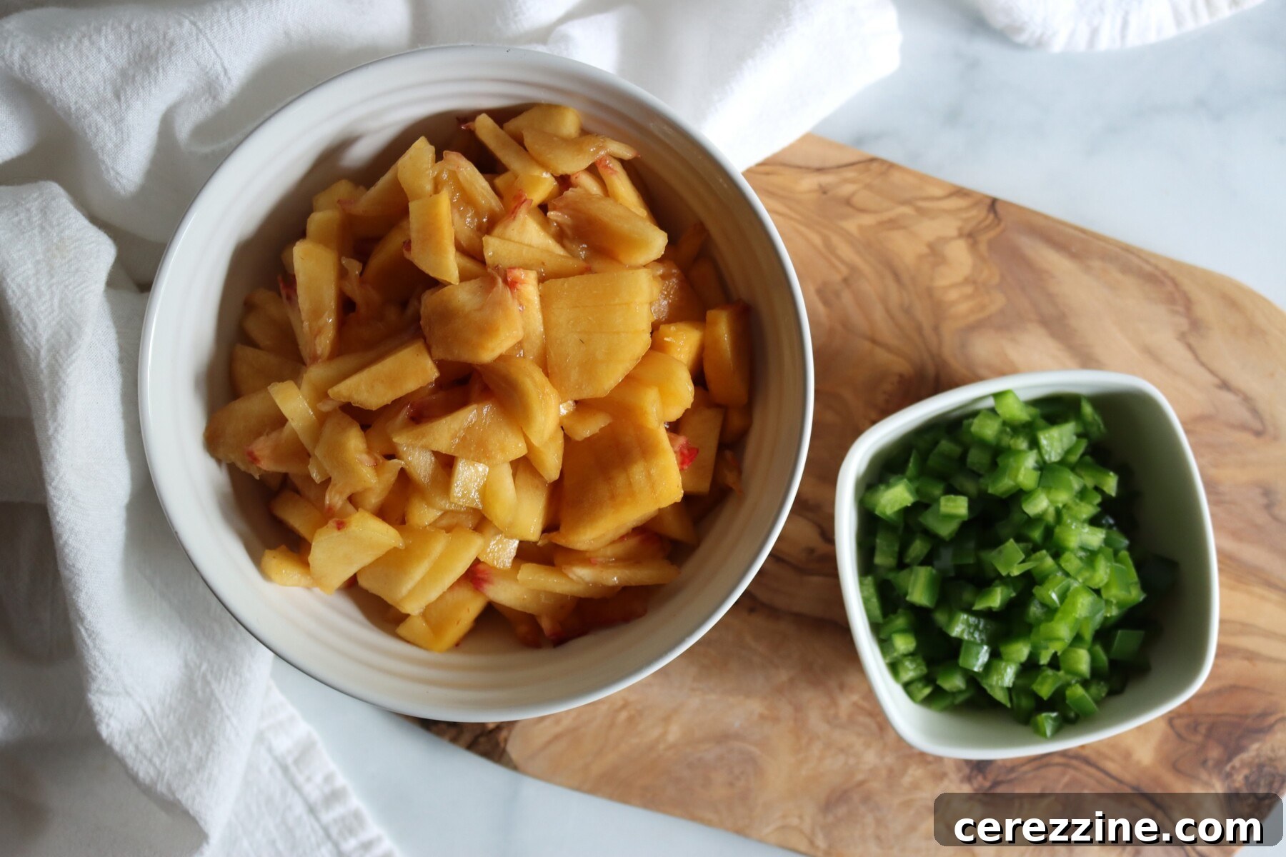 Chopped peeled peaches and finely chopped jalapeños in bowls, ready for peach jalapeño jam