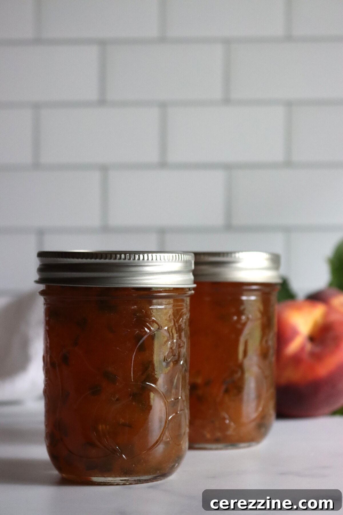 Close-up of peach jalapeño jam in jars, with green flecks of jalapeño through the peaches
