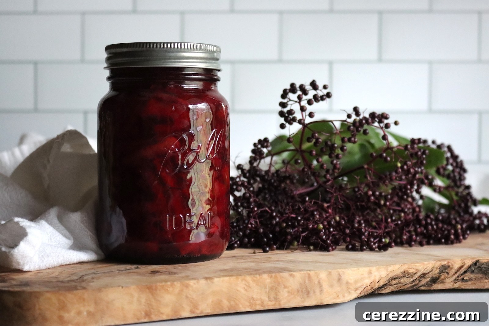Jar of elderberry marmalade on a wooden board with fresh elderberry clusters behind it