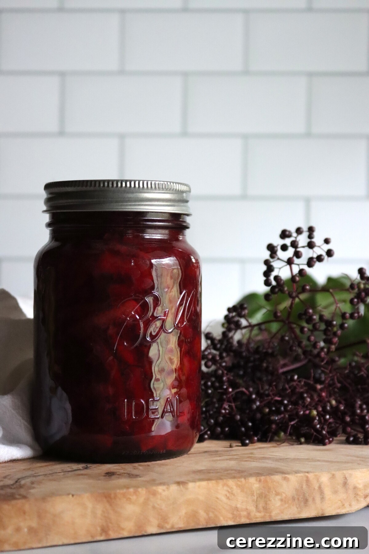 Jar of homemade elderberry marmalade with fresh elderberries on an olive wood board