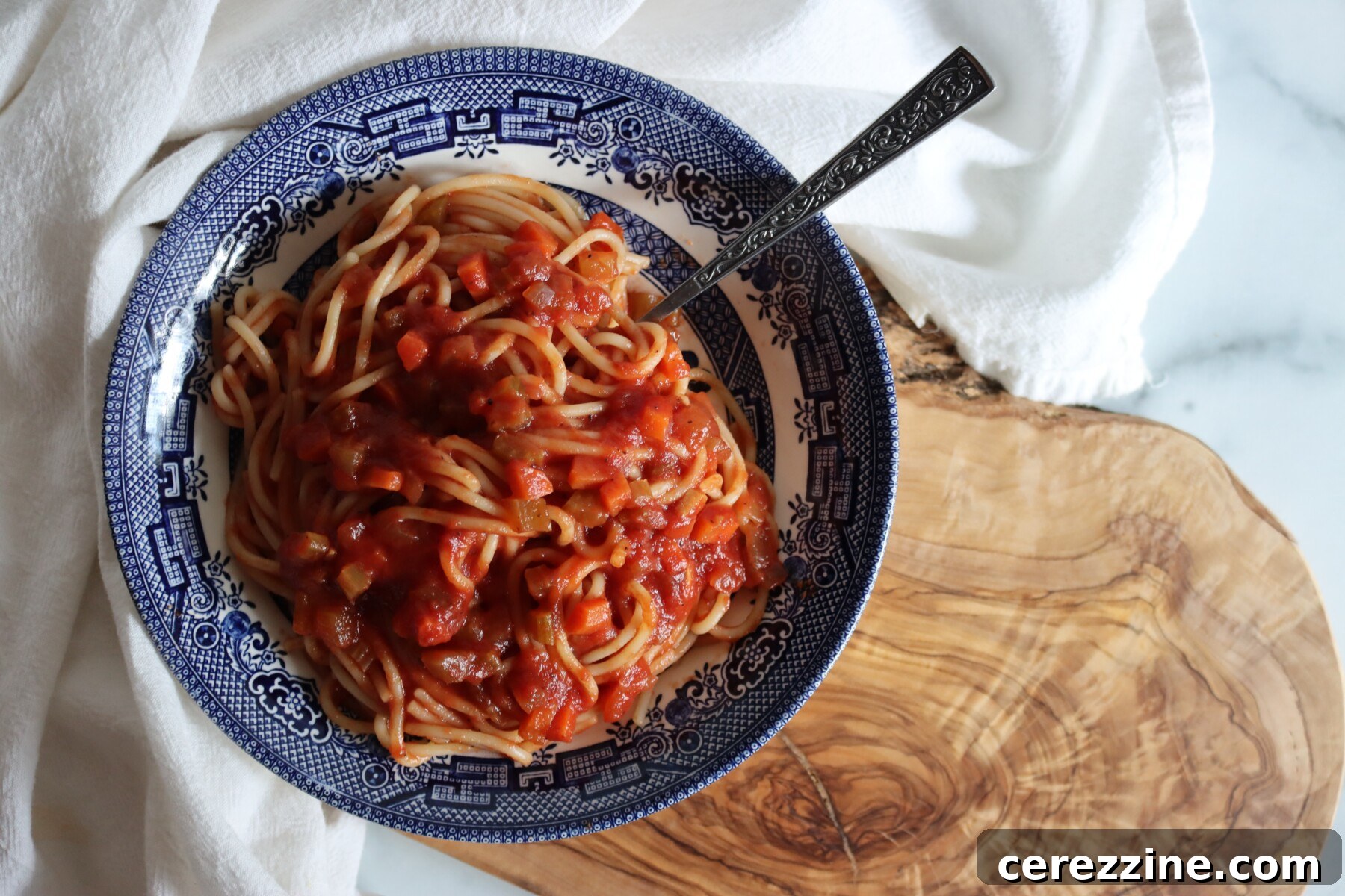 Spaghetti with homemade Italian tomato sauce in a blue and white bowl on an olive wood board