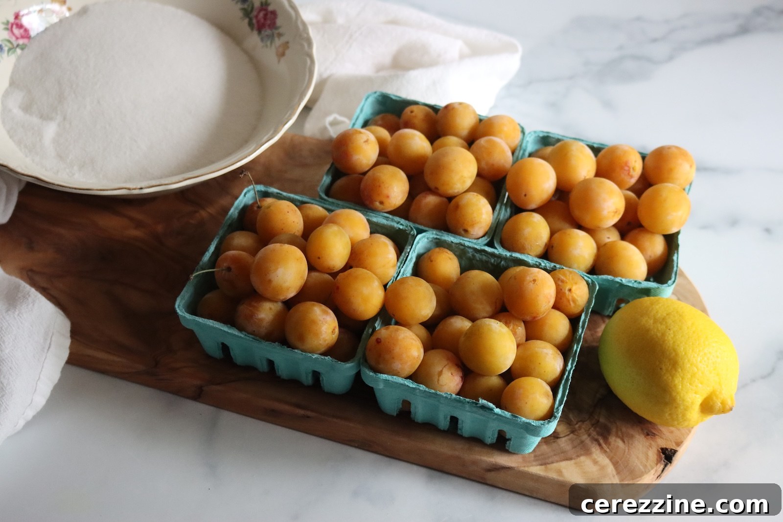 Fresh mirabelle plums in berry baskets with a bowl of sugar and a lemon