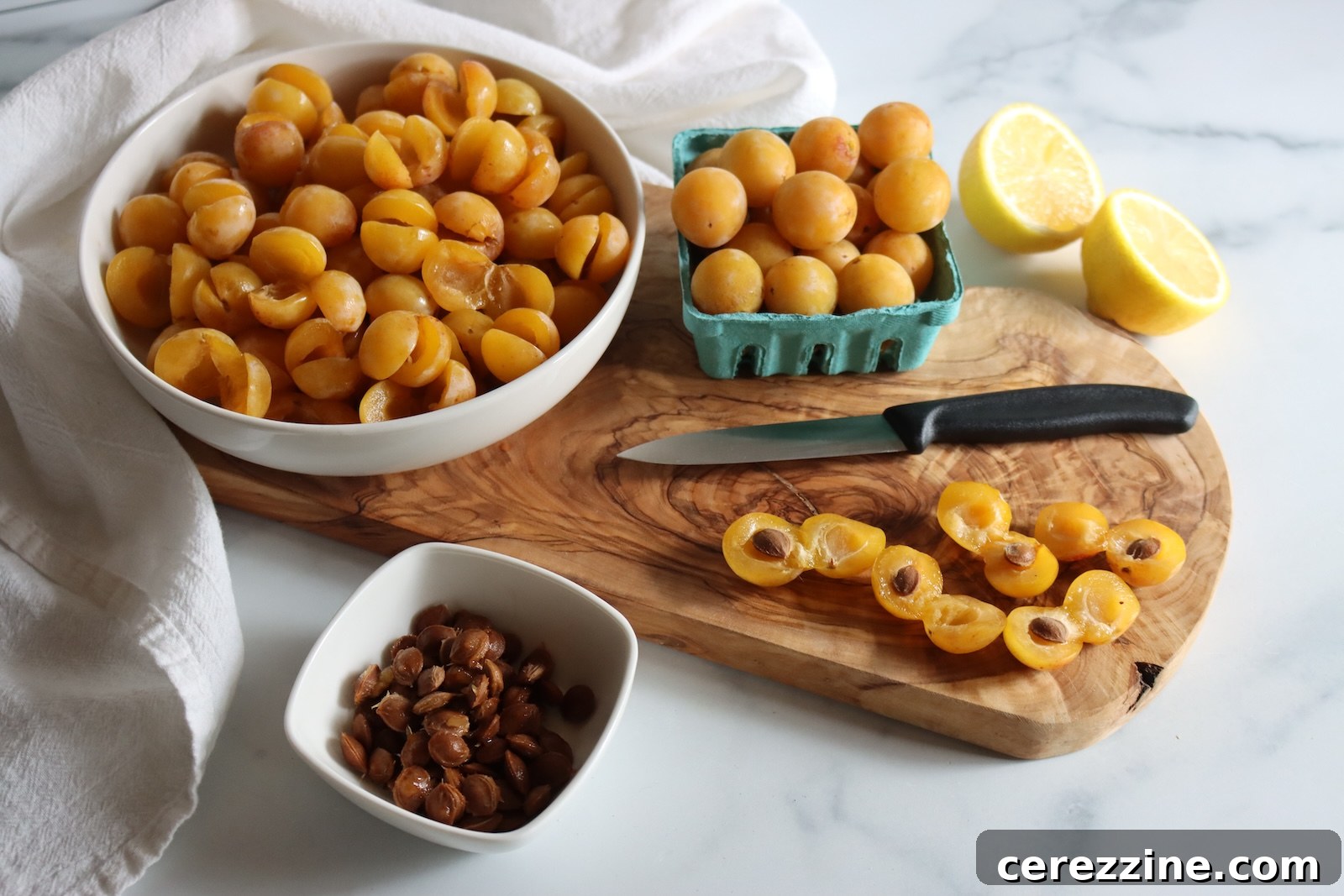 Mirabelle plums sliced in half and pitted, with a paring knife and a bowl of pits