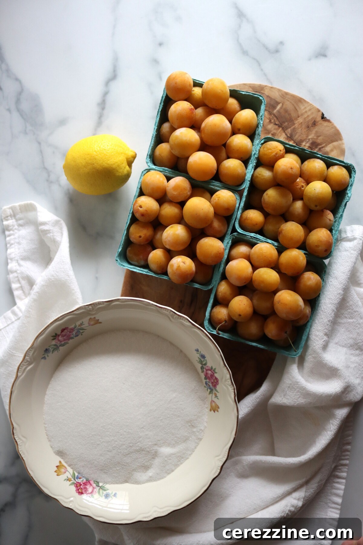 Mirabelle plums in green berry baskets with sugar and a lemon on a marble counter