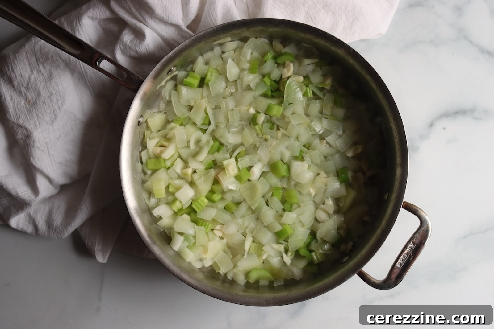 Diced onions and celery softening in a stainless steel pan