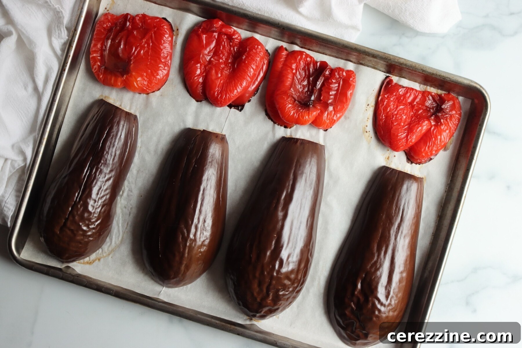 Eggplant quarters and red pepper halves roasted skin side up on a sheet pan for caponata